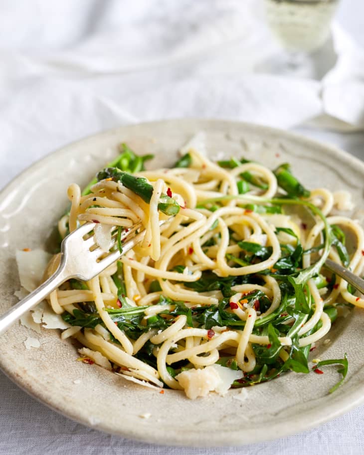 Spaghetti with arugula, red pepper flakes, and shaved parmesan on a beige plate.