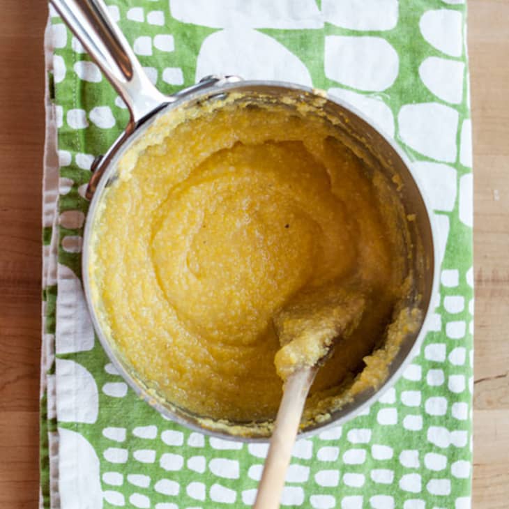 Pot of creamy polenta with a wooden spoon on a green patterned cloth.