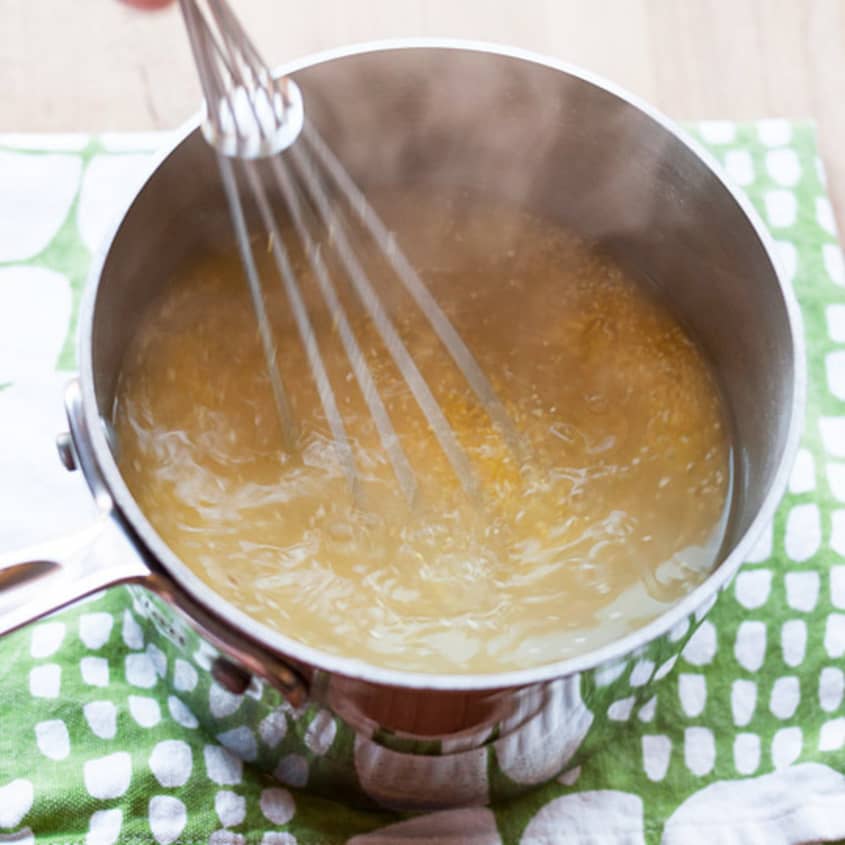 Whisk stirring creamy polenta in a saucepan on a green patterned cloth.