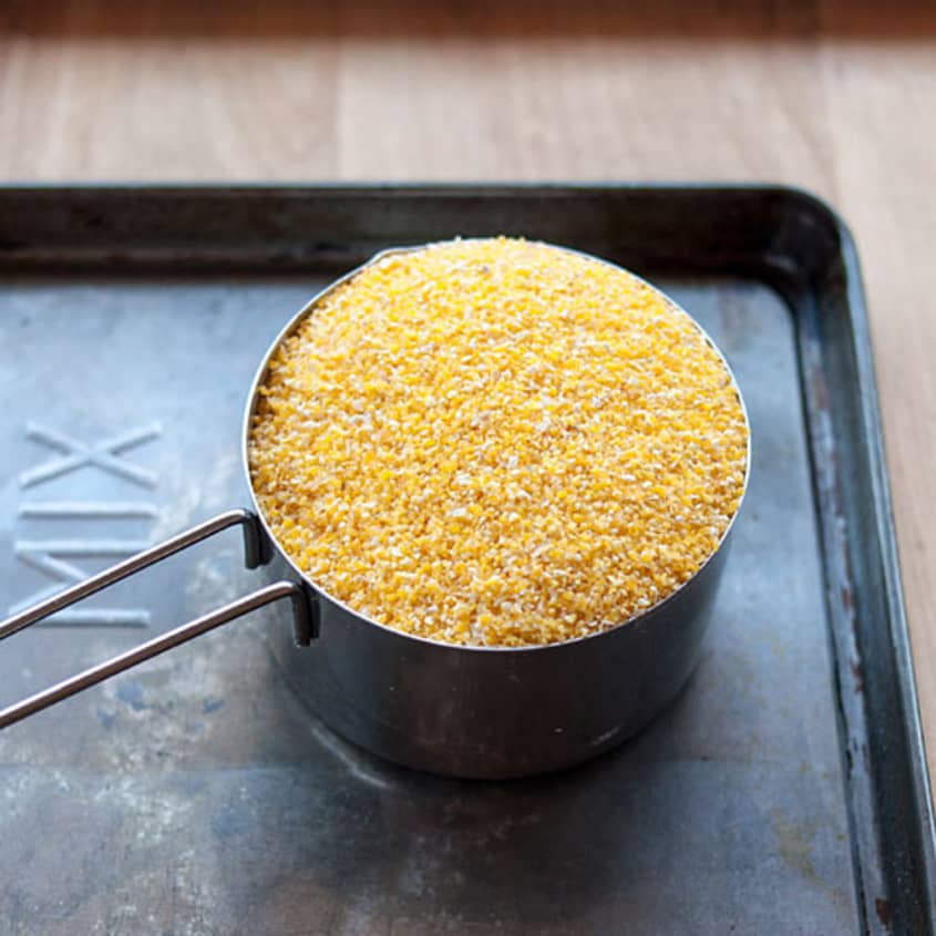 Measuring cup filled with yellow cornmeal on a baking sheet.