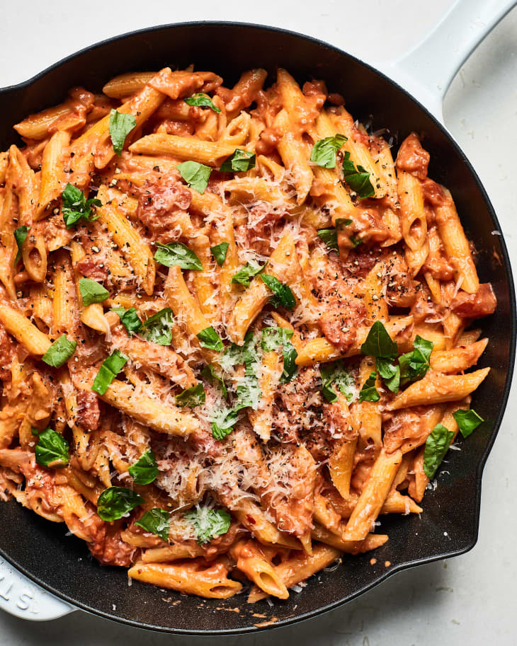 Creamy tomato pasta with penne, fresh basil, and grated cheese in a skillet.