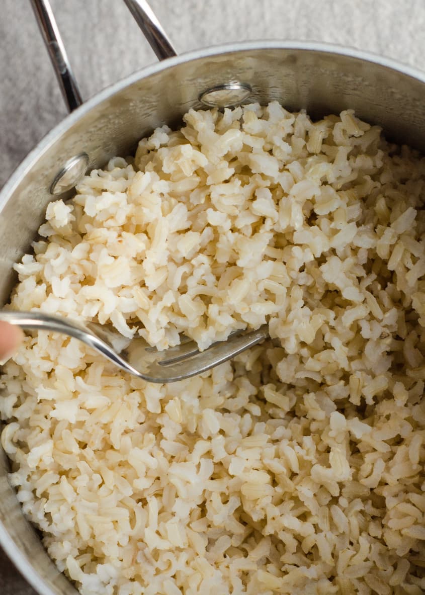 Cooked brown rice in a stainless steel pot being fluffed with a fork.