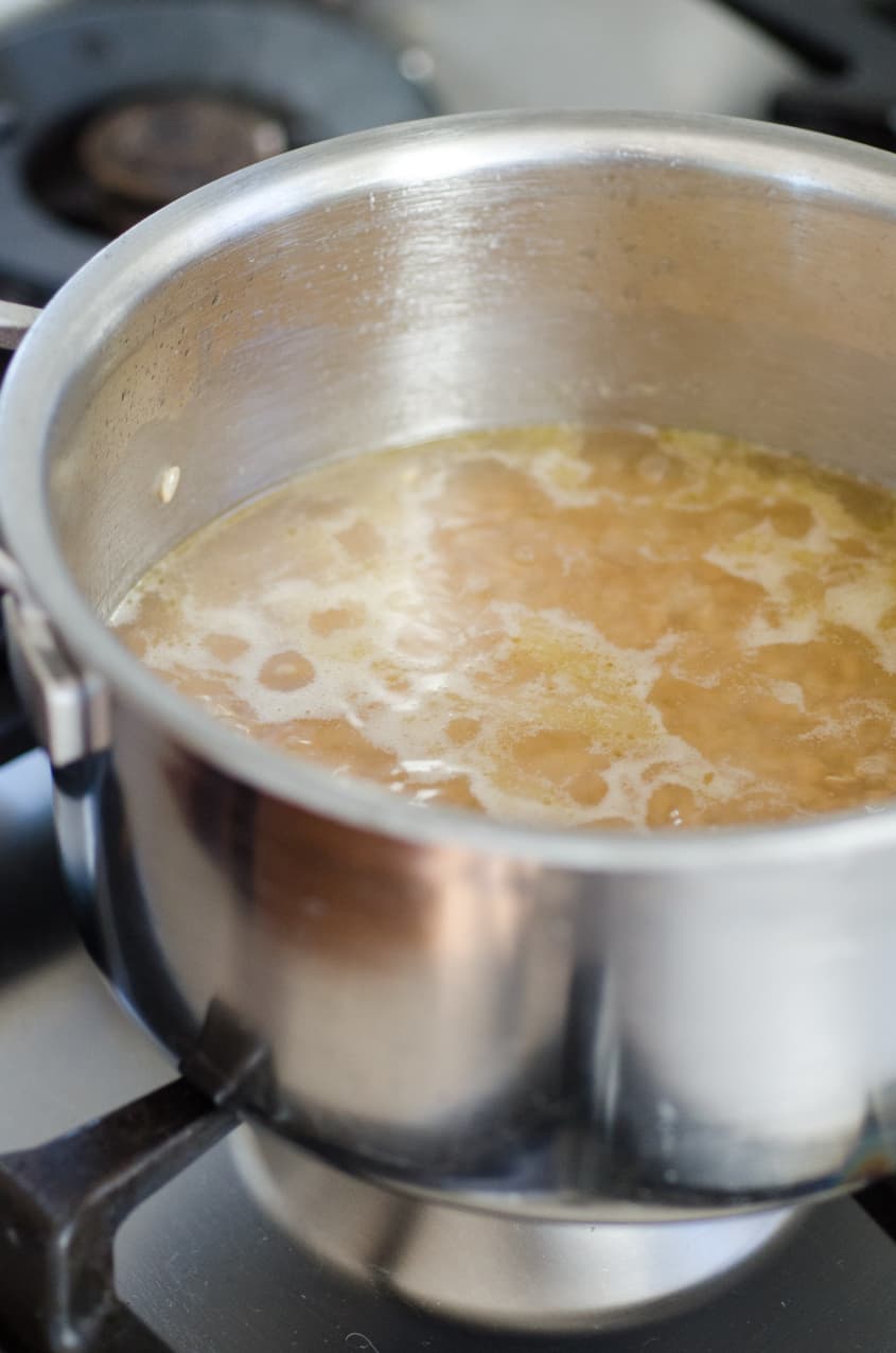 Brown rice simmering in a stainless steel pot on a stovetop.
