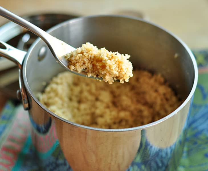 Cooked couscous in a saucepan with a spoon lifting a portion.