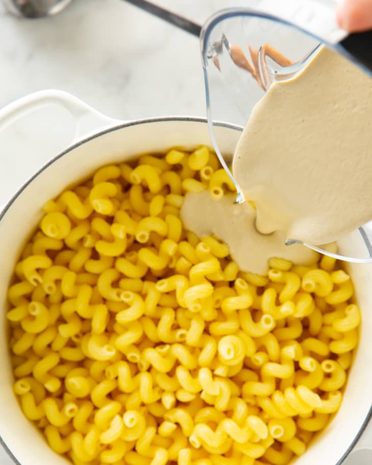 Pouring creamy sauce over cooked cavatappi pasta in a white pot.