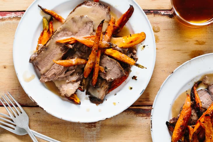 Roast beef slices with glazed carrots and gravy on a white plate, set on a wooden table.