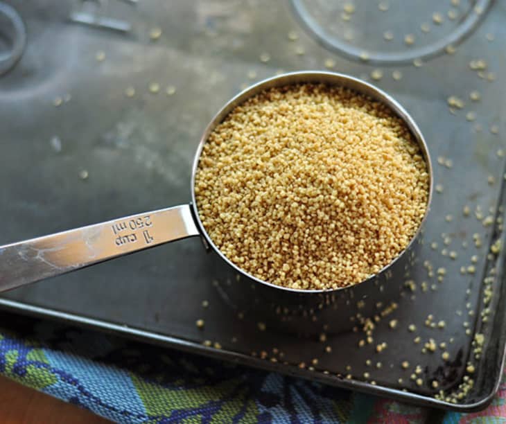 Measuring cup filled with uncooked couscous on a baking sheet.