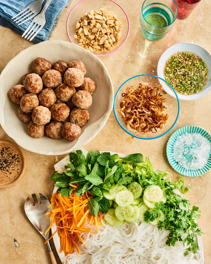 Vermicelli noodles with lemongrass pork meatballs, fresh herbs, cucumber, carrots, and peanuts on a table.