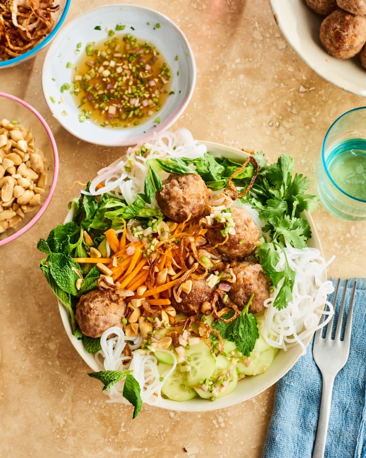 Bowl of vermicelli noodles with meatballs, carrots, cucumbers, mint, cilantro, and peanuts, served with dipping sauce.