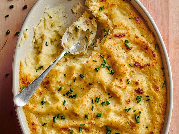 Baked mashed potatoes in an oval dish, topped with chopped chives and a serving spoon.