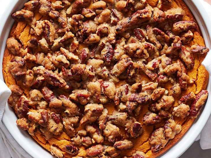 Someone holding dish of sweet potato souffle topped with pecans.