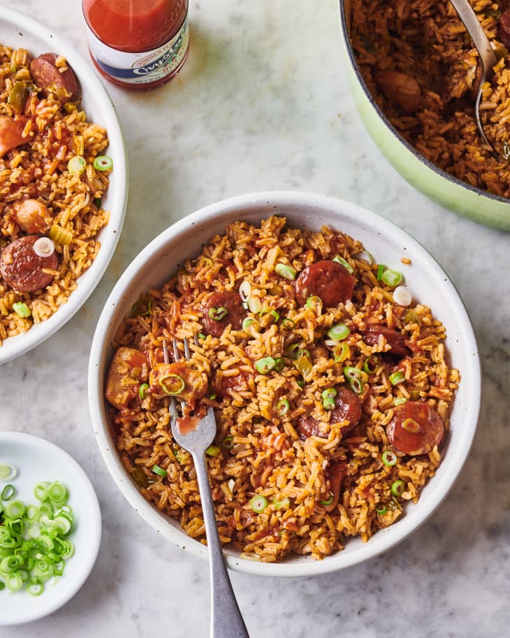 two bowls of jambalaya on a table near hot sauce