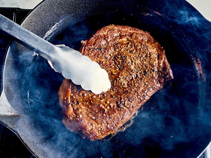 a steak being seared in a skillet