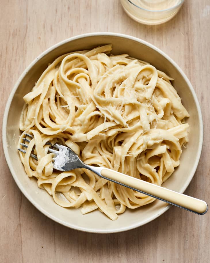 Bowl of creamy fettuccine pasta with a fork on a wooden table.
