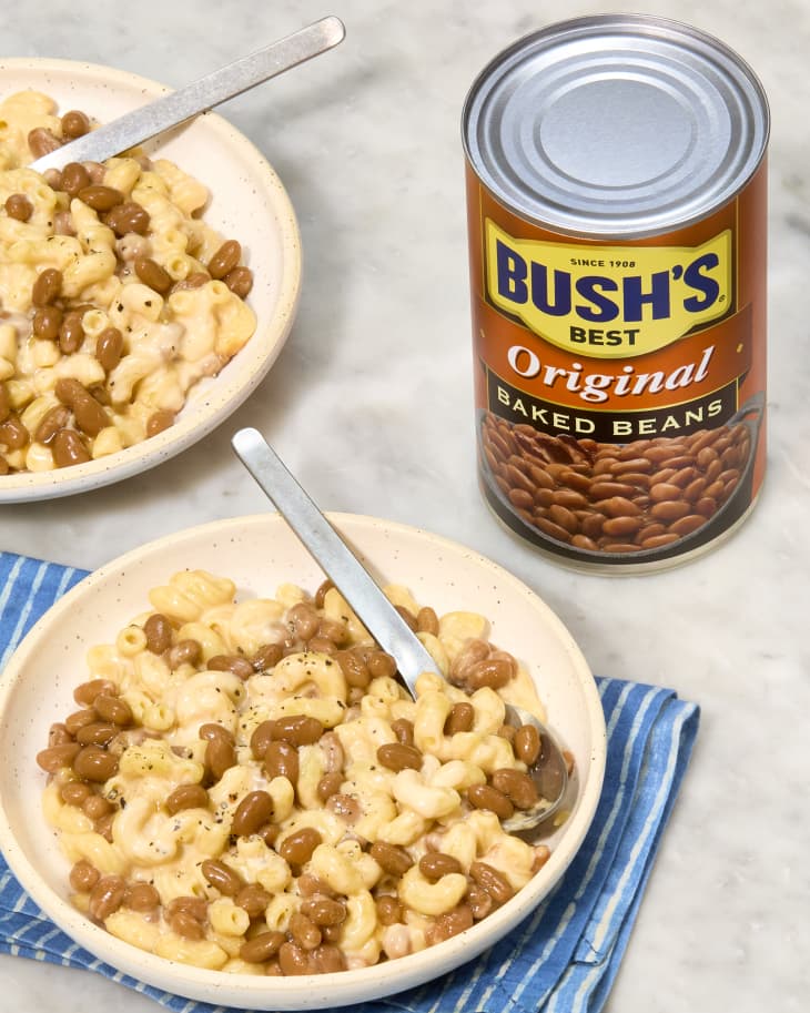 Mac and cheese with baked beans in bowls, next to a can of Bush's Original Baked Beans on a blue striped cloth.