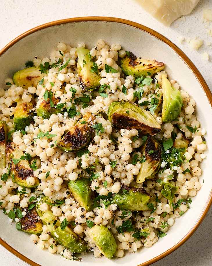 Creamy pearl couscous mixed with roasted Brussels sprouts and fresh parsley, garnished with black pepper.