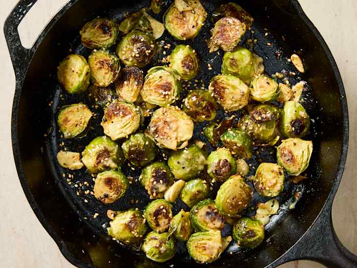 Sautéed Brussels sprouts with garlic and sesame seeds in a cast iron skillet.