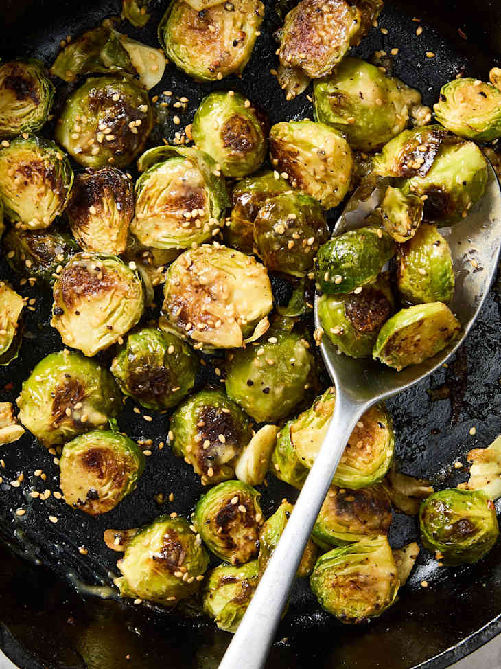 Sautéed Brussels sprouts with garlic and sesame seeds in a cast iron skillet.