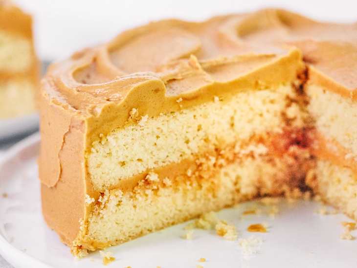 Layered cake with smooth caramel frosting, revealing a soft sponge interior and a hint of filling.