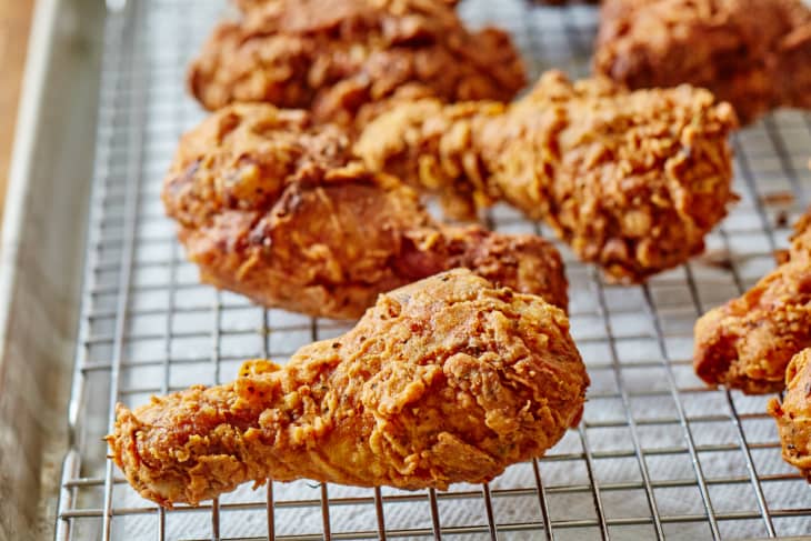 Pieces of fried chicken drying on rack over paper towel-lined sheet pan