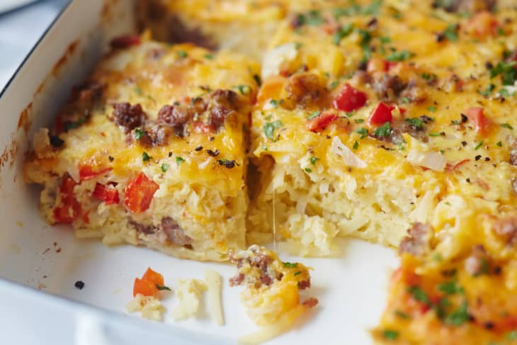 Cheesy breakfast casserole with sausage, red peppers, and herbs in a baking dish.