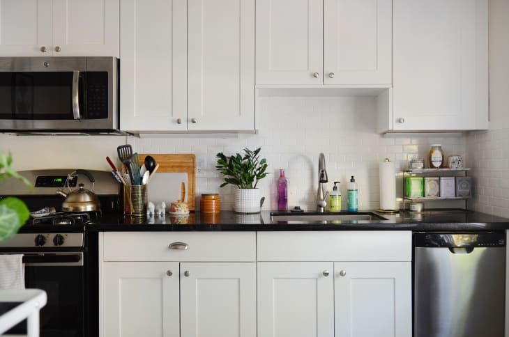 Modern kitchen with white cabinets, black countertop, stainless steel appliances, and potted plant near the sink.