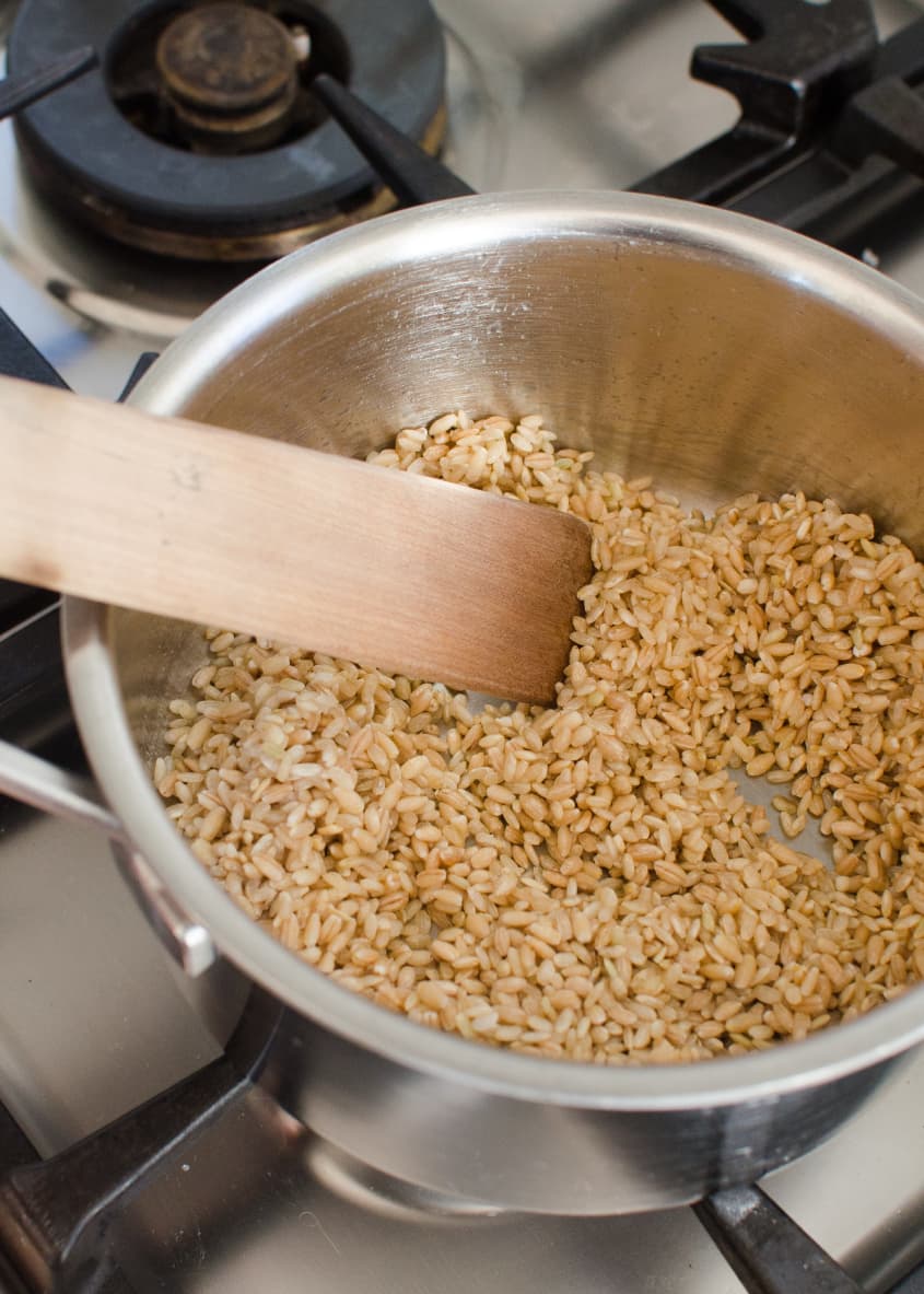 Brown rice being stirred in a stainless steel pot on a stove.