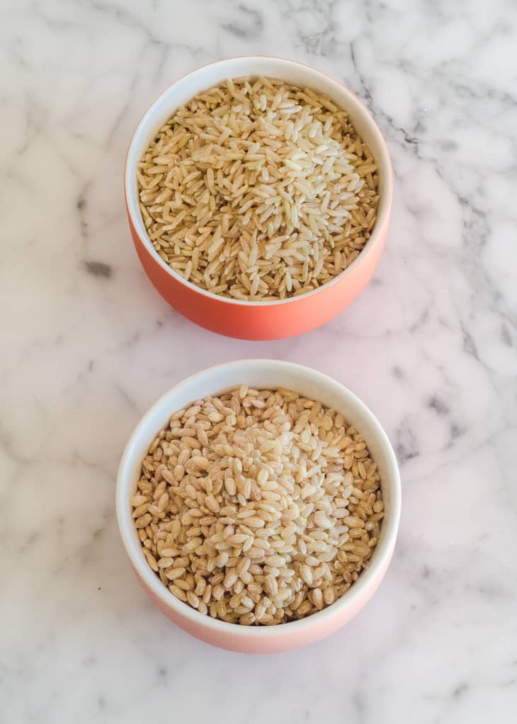 Two bowls of uncooked brown rice on a marble surface.
