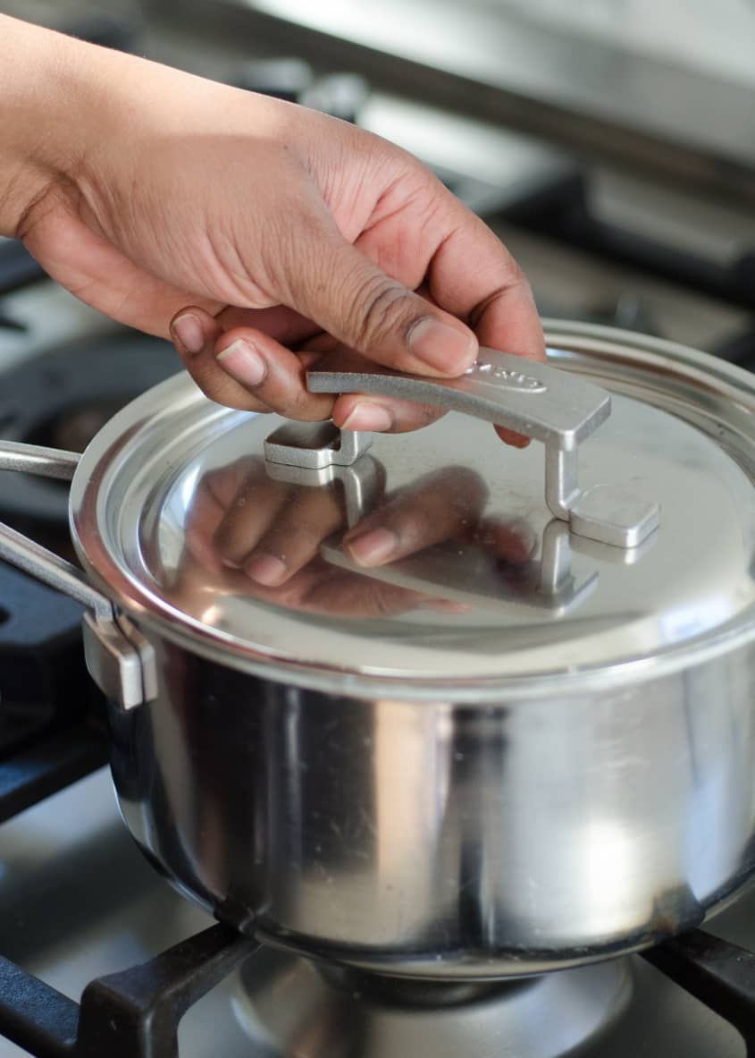 Hand placing lid on a stainless steel pot on a stove, related to cooking brown rice.