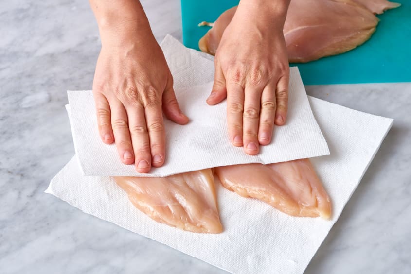 Patting raw chicken breasts dry with paper towels on a marble surface.