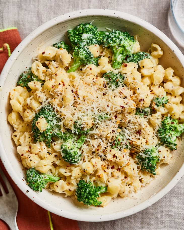 Creamy pasta shells with broccoli, topped with grated cheese and red pepper flakes in a white bowl.