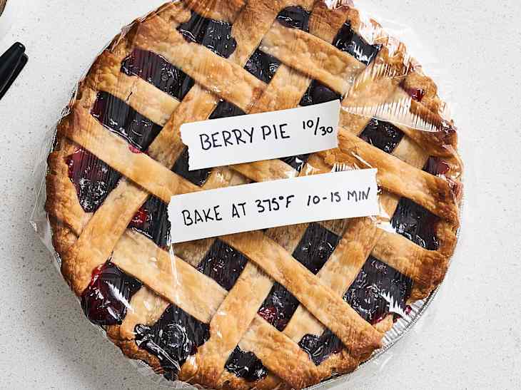 Berry pie covered in plastic wrap with baking instructions on paper labels.