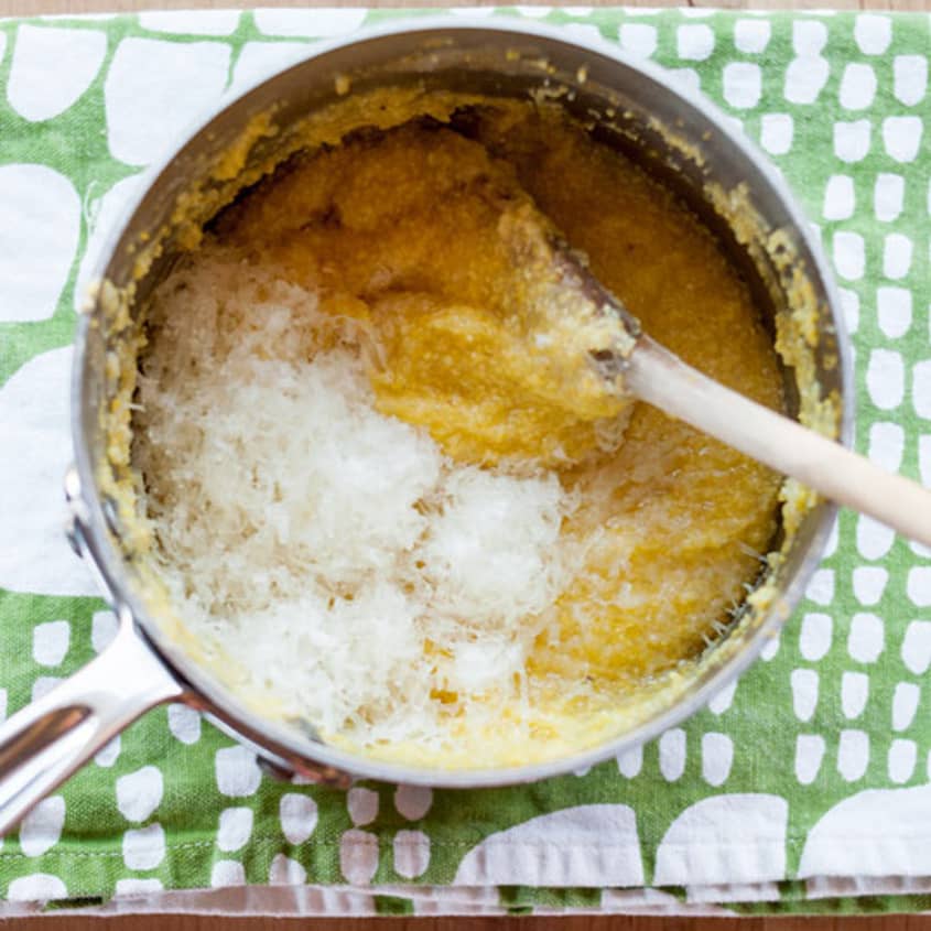 Creamy stovetop polenta in a saucepan with grated cheese on a green patterned cloth.