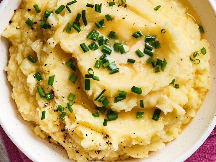 Creamy mashed potatoes topped with chopped chives and black pepper in a white bowl.