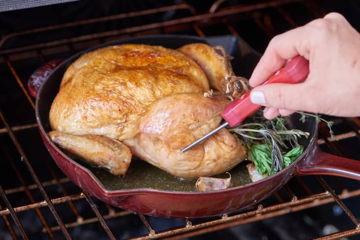 Testing a roasting chicken for doneness by inserting a thermometer into a thigh.