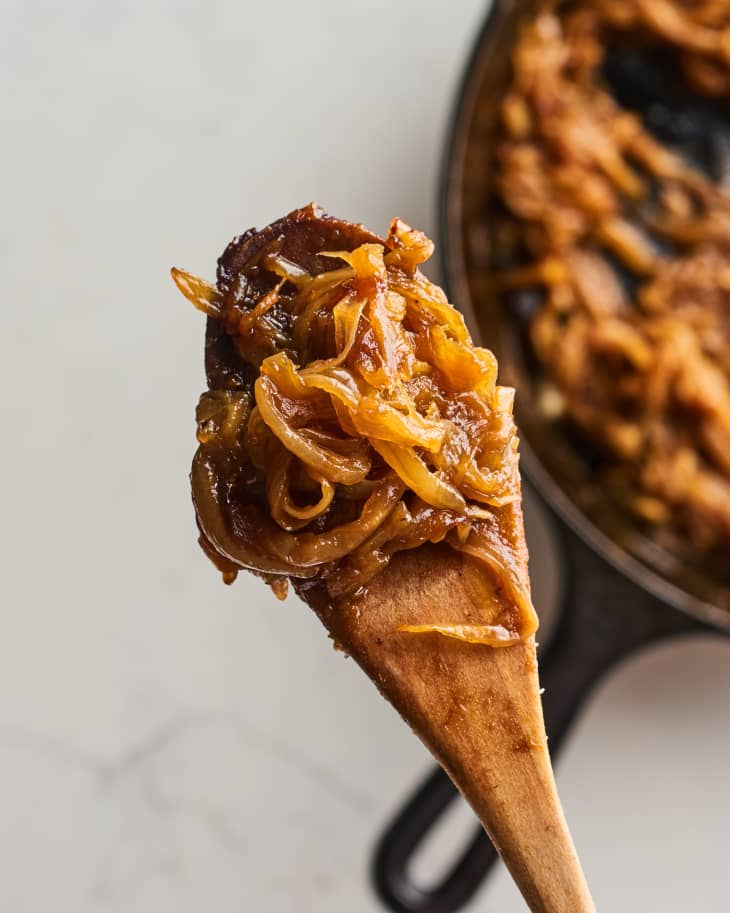 Caramelized onions on a wooden spoon with a skillet in the background.