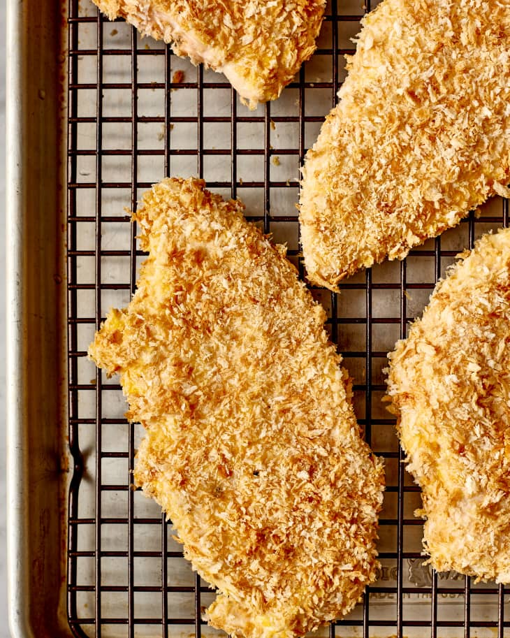 Breaded chicken breasts on a wire rack over a baking sheet.