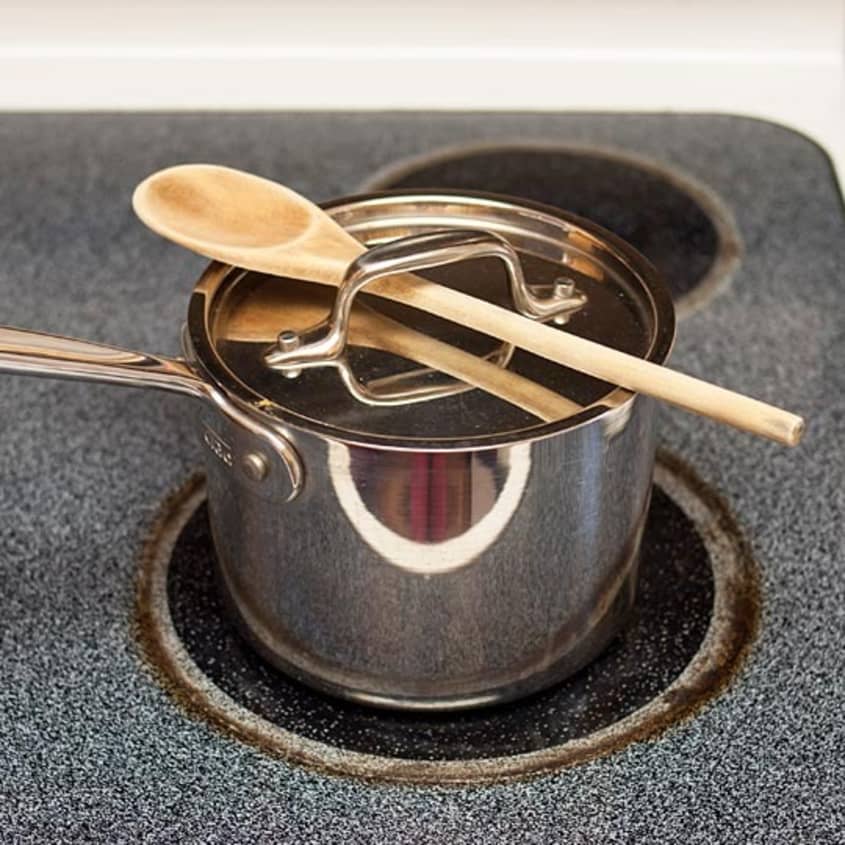 A stainless steel pot with a wooden spoon on a stovetop, ready for cooking polenta.