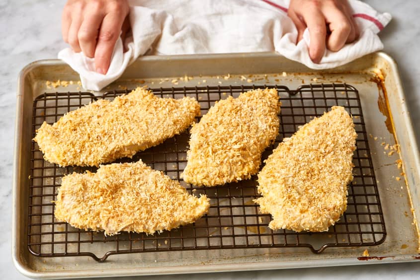 Four baked Parmesan-crusted chicken breasts on a wire rack over a baking sheet.
