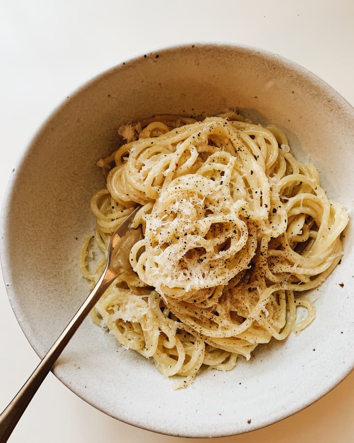 Spaghetti coated in creamy sauce with grated cheese and black pepper in a beige bowl.