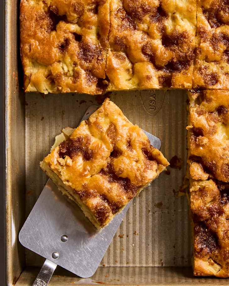 Cinnamon coffee cake squares in a baking pan with a metal spatula lifting a piece.