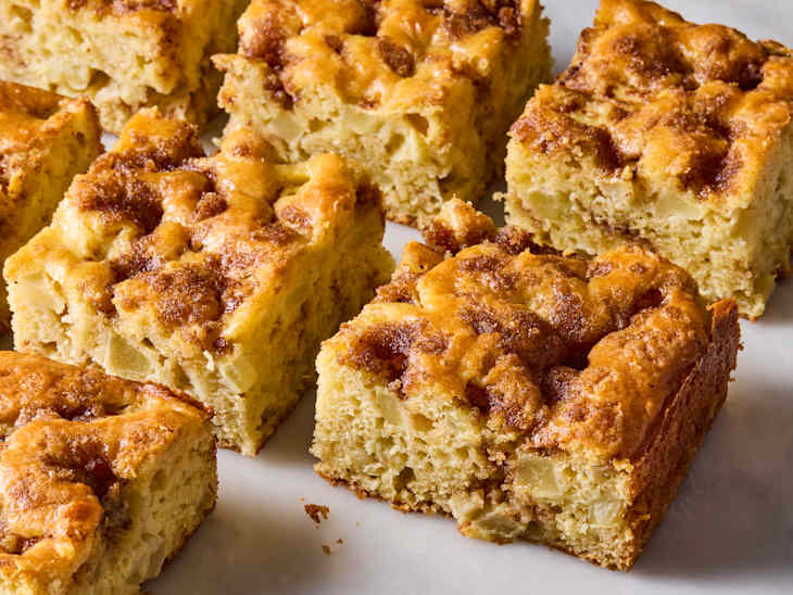 Squares of apple cake with a golden-brown top, showing chunks of apple and a crumbly texture.