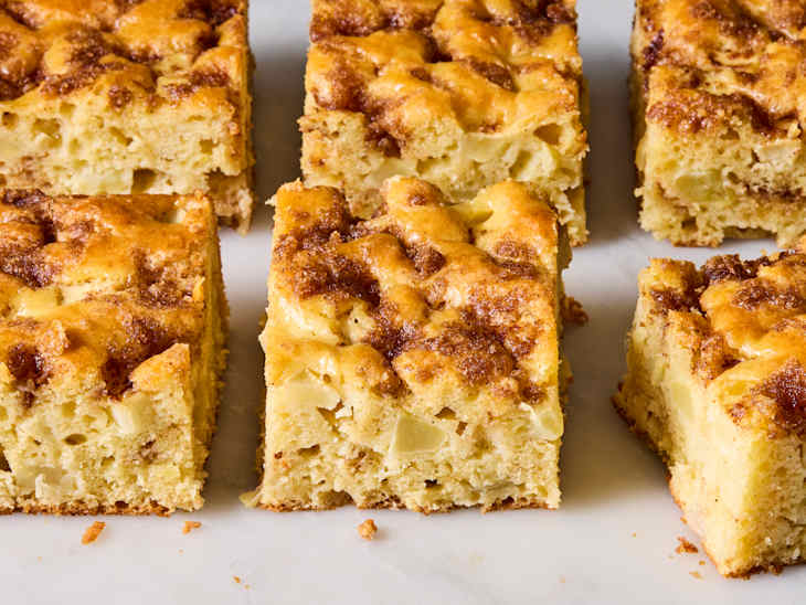 Sliced apple cake with a golden-brown top, showing moist texture and apple pieces throughout.