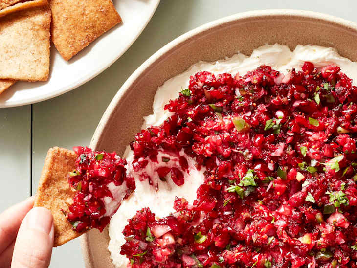 Someone dipping pita chip into cranberry jalapeno dip.