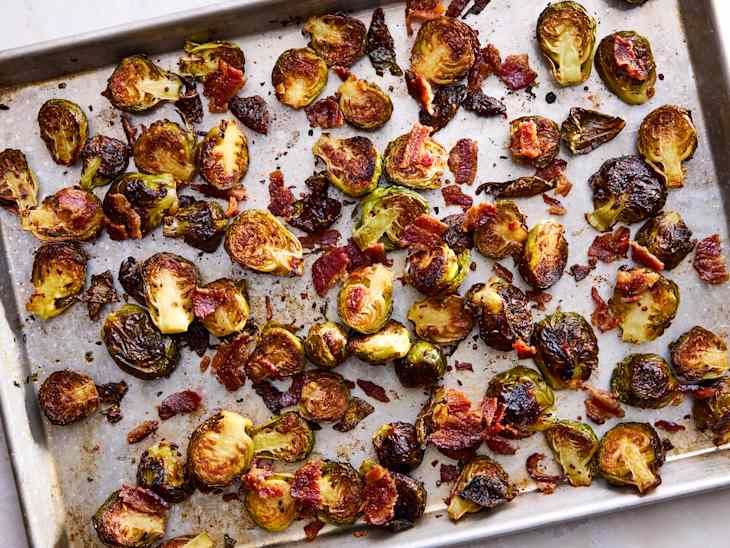 Roasted Brussels sprouts mixed with crispy bacon on a baking sheet, showcasing a golden-brown and charred appearance.