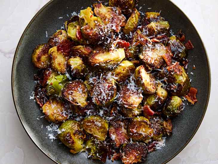 Roasted Brussels sprouts with crispy bacon and grated cheese on a dark plate.