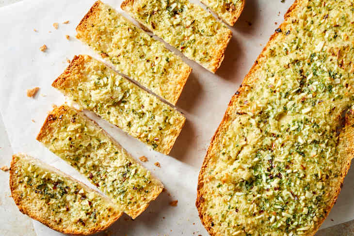 Overhead shot of two loaves of garlic bread, the loaf on the left is sliced into six slices.