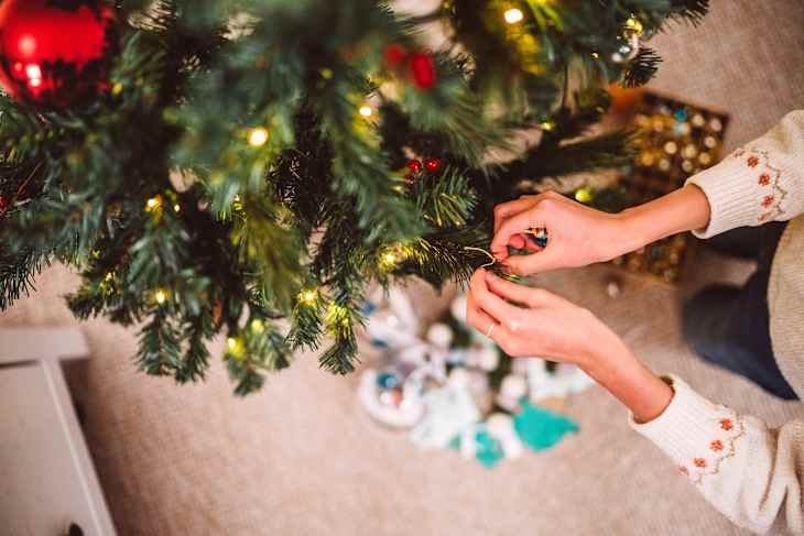 A close-up shot of hands decoration decorating Christmas tree at home in festive holiday