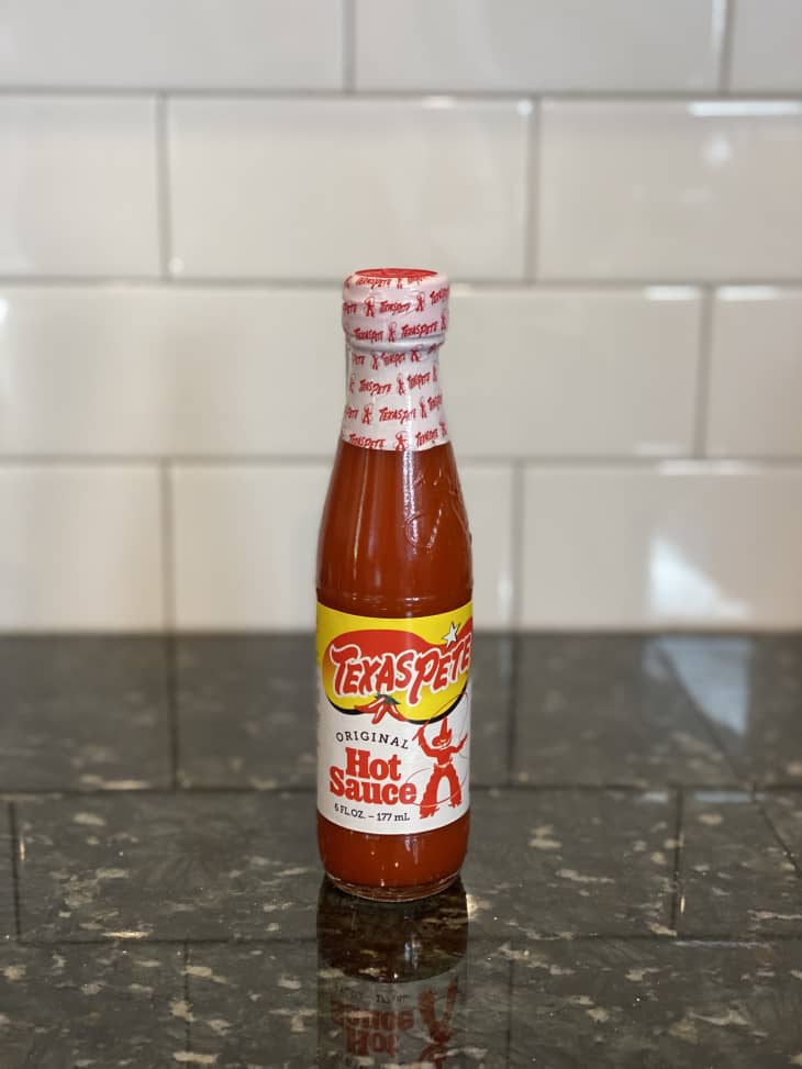 Texas Pete Original Hot Sauce bottle on a dark granite countertop with white subway tile backsplash.