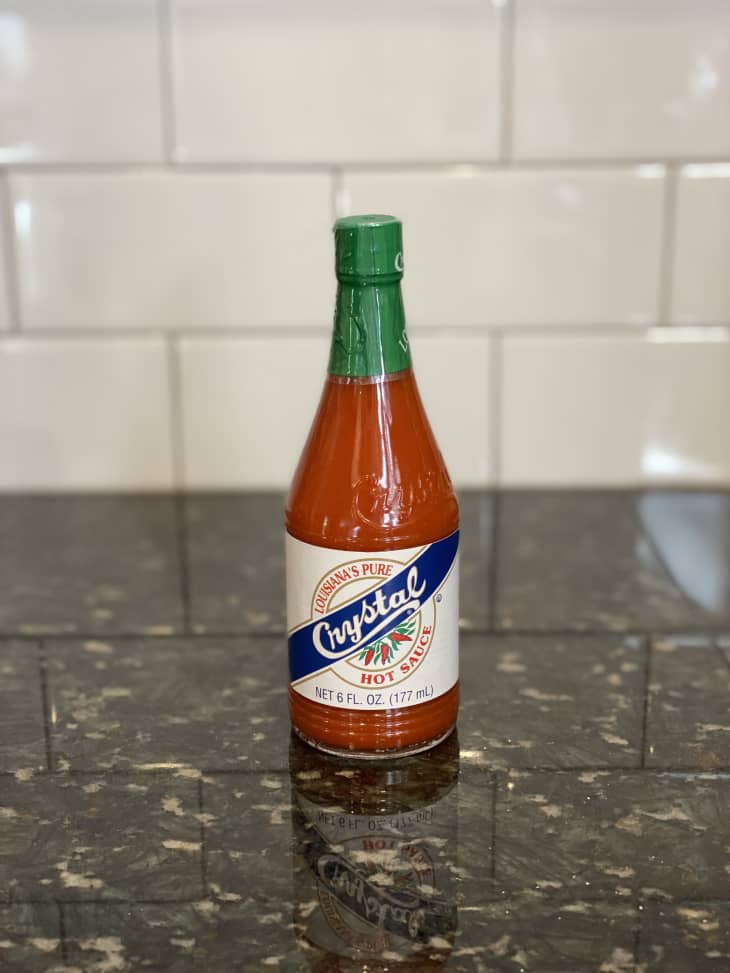 Crystal hot sauce bottle on a dark granite countertop with white tile backsplash.